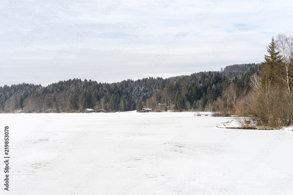 Shore of frozen Kirchsee lake with boating huts, Bavaria, in winter