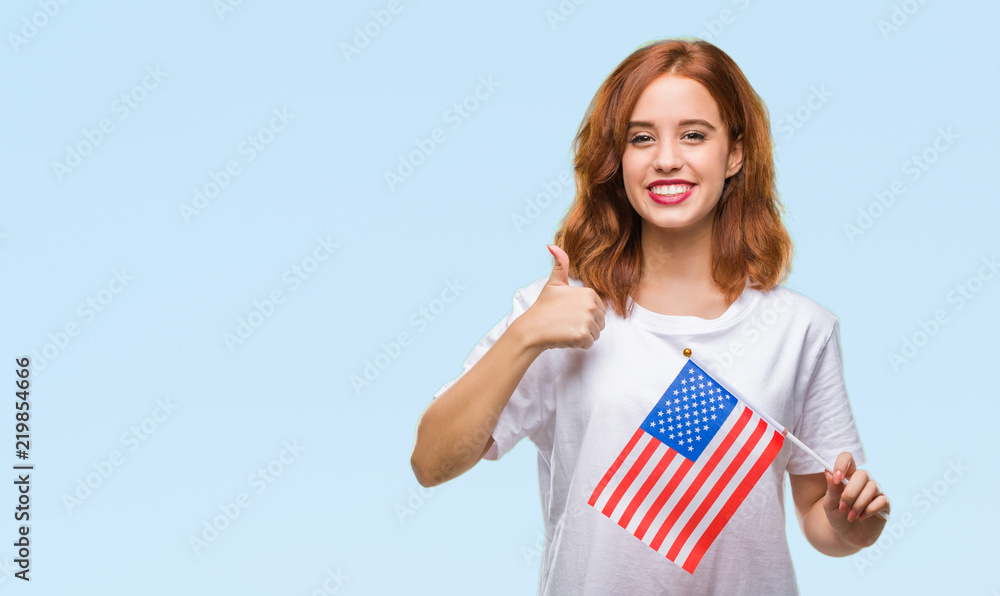 Young beautiful woman holding flag of america over isolated background happy with big smile doing ok sign, thumb up with fingers, excellent sign Young beautiful woman holding flag of america over isolated background happy with big smile doing ok sign, thumb up with fingers, excellent sign