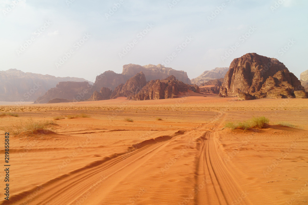 Wadi Rum desert, Jordan, Middle East, known as The Valley of the Moon.  Orange sand, blue sky, haze and clouds. Designation as a UNESCO World Heritage Site. Red planet Mars landscape.