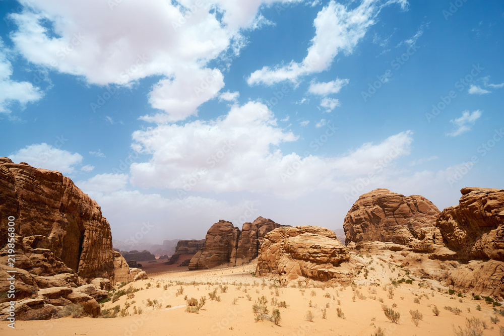 Wadi Rum desert, Jordan, Middle East, The Valley of the Moon. Orange sand, haze, clouds. Designation as a UNESCO World Heritage Site. National park Offroad adventures travel background. Wadi Rum desert, Jordan, Middle East, The Valley of the Moon. Orange sand, haze, clouds. Designation as a UNESCO World Heritage Site. National park Offroad adventures travel background.