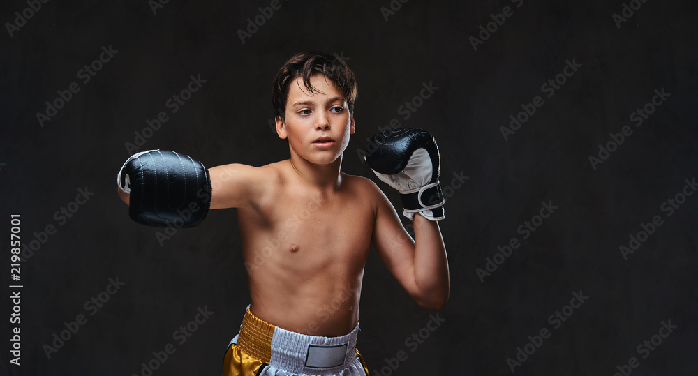 Handsome shirtless young boxer during boxing exercises, focused on process with serious concentrated facial. Isolated on the dark background.