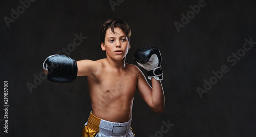 Handsome shirtless young boxer during boxing exercises, focused on process with serious concentrated facial. Isolated on the dark background. © Fxquadro