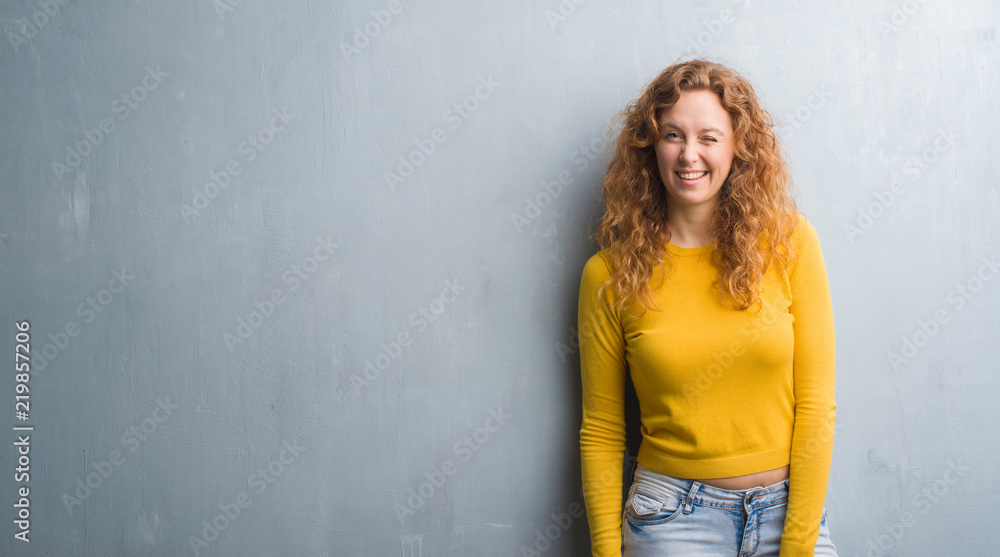 Young redhead woman over grey grunge wall winking looking at the camera with sexy expression, cheerful and happy face. Young redhead woman over grey grunge wall winking looking at the camera with sexy expression, cheerful and happy face.