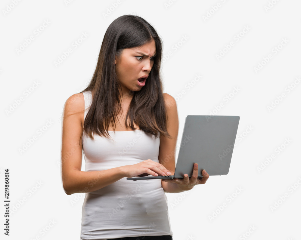 Young hispanic woman using computer laptop scared in shock with a surprise face, afraid and excited with fear expression Young hispanic woman using computer laptop scared in shock with a surprise face, afraid and excited with fear expression