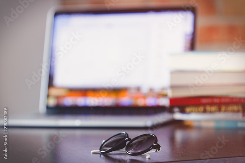 sunglasses on a table with laptop computer and books on brick wall background