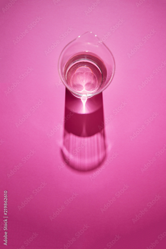 Clean glass with water on a pink paper background with shadows. Clean glass with water on a pink paper background with shadows.