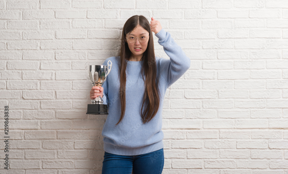 Young Chinese woman holding trophy annoyed and frustrated shouting with anger, crazy and yelling with raised hand, anger concept Young Chinese woman holding trophy annoyed and frustrated shouting with anger, crazy and yelling with raised hand, anger concept