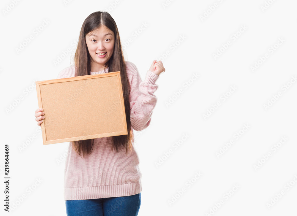 Young Chinese woman over isolated background holding corkboard screaming proud and celebrating victory and success very excited, cheering emotion Young Chinese woman over isolated background holding corkboard screaming proud and celebrating victory and success very excited, cheering emotion