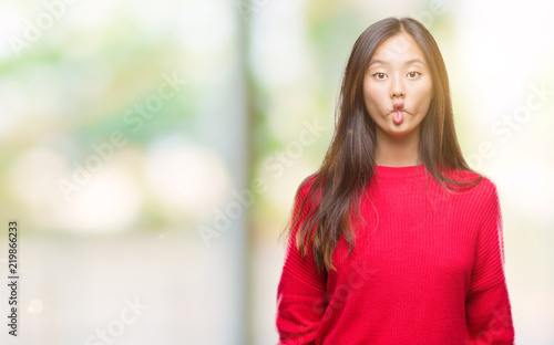 Young asian woman wearing winter sweater over isolated background making fish face with lips, crazy and comical gesture. Funny expression.