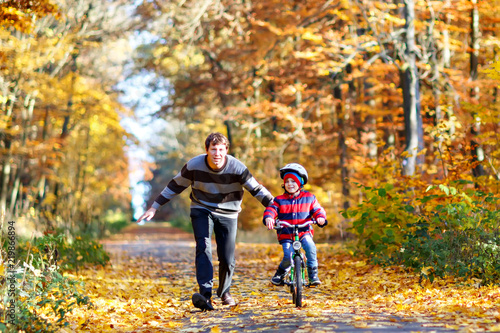 Little preschool kid boy and his father in autumn park with a bicycle. Dad teaching his son biking. Active family leisure. Child with helmet on bike. Safety, sports, leisure with kids concept..