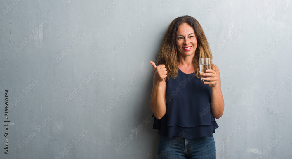 Middle age hispanic woman drinking glass of water happy with big smile doing ok sign, thumb up with fingers, excellent sign Middle age hispanic woman drinking glass of water happy with big smile doing ok sign, thumb up with fingers, excellent sign