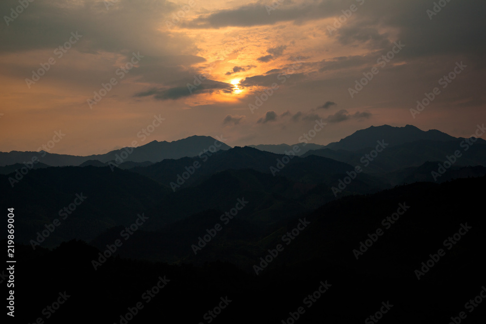 Sunset Abstract Graphic Resource. Panoramic Mountains, Clouds and Sun behind clouds in the shape of an orange lowing ball, opening in the clouds. Sign from heaven concept, calm mountains sundown.