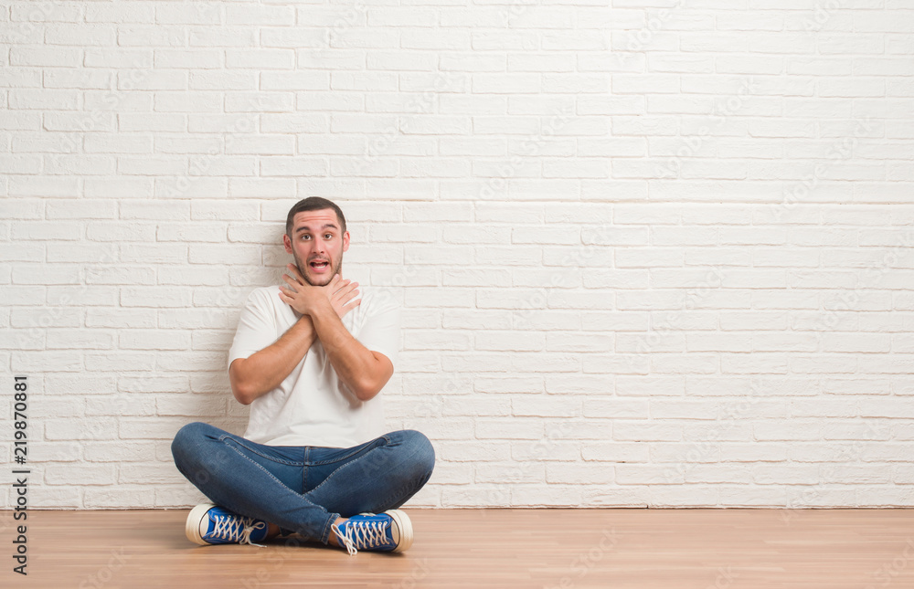 Young caucasian man sitting on the floor over white brick wall shouting and suffocate because painful strangle. Health problem. Asphyxiate and suicide concept. Young caucasian man sitting on the floor over white brick wall shouting and suffocate because painful strangle. Health problem. Asphyxiate and suicide concept.