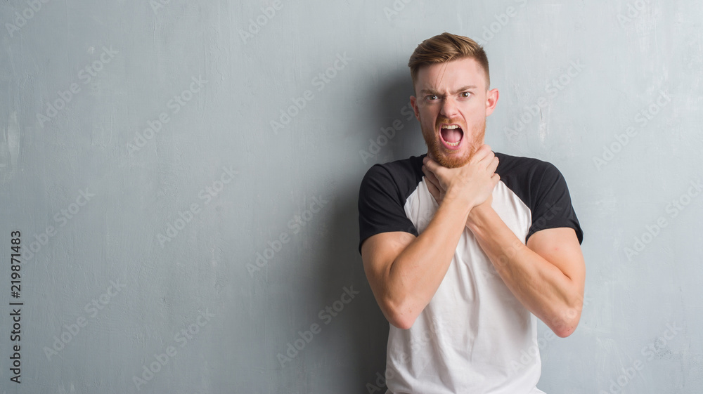 Young redhead man over grey grunge wall shouting and suffocate because painful strangle. Health problem. Asphyxiate and suicide concept. Young redhead man over grey grunge wall shouting and suffocate because painful strangle. Health problem. Asphyxiate and suicide concept.