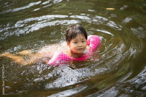 Fototapeta Naklejka Na Ścianę i Meble -  little asian girl wearing inflatable sleeves swimming in nature water on holiday