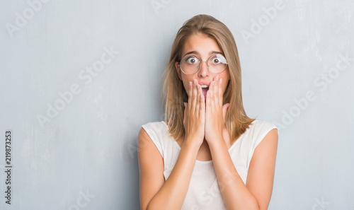Canvastavla Beautiful young woman standing over grunge grey wall wearing glasses cover mouth