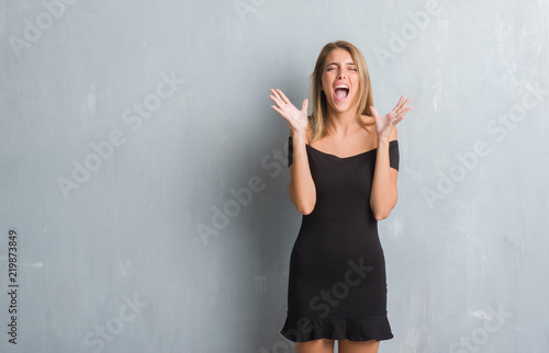 Beautiful young woman standing over grunge grey wall wearing elegant dress celebrating mad and crazy for success with arms raised and closed eyes screaming excited. Winner concept © Krakenimages.com