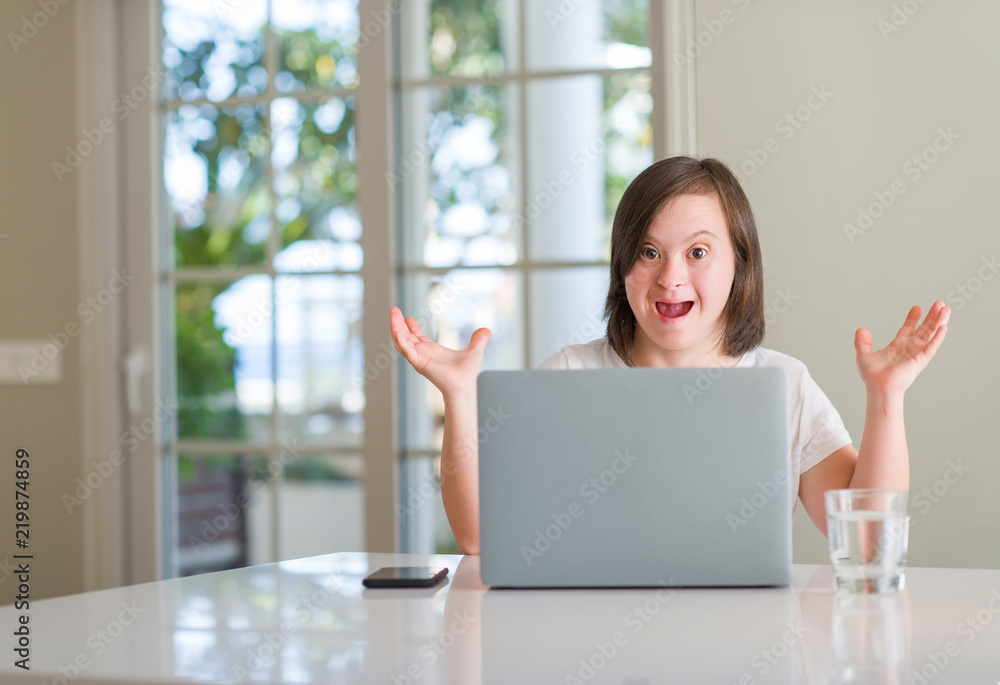Down syndrome woman at home using computer laptop very happy and excited, winner expression celebrating victory screaming with big smile and raised hands