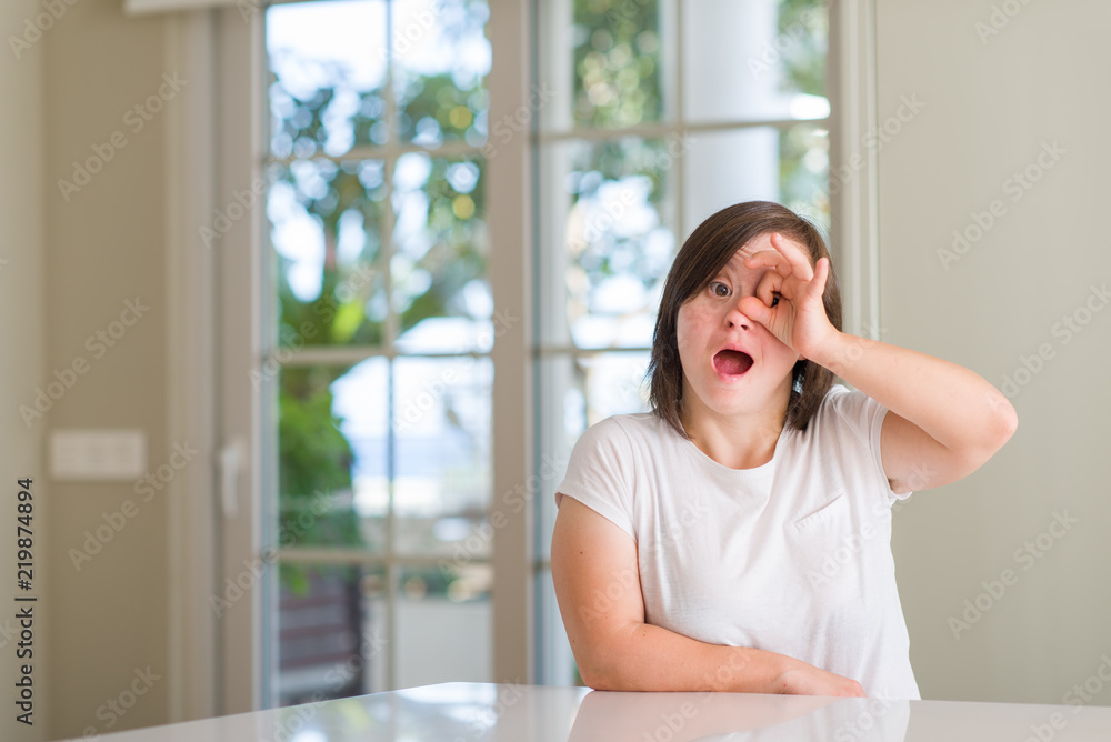 Down syndrome woman at home doing ok gesture shocked with surprised face, eye looking through fingers. Unbelieving expression. Down syndrome woman at home doing ok gesture shocked with surprised face, eye looking through fingers. Unbelieving expression.