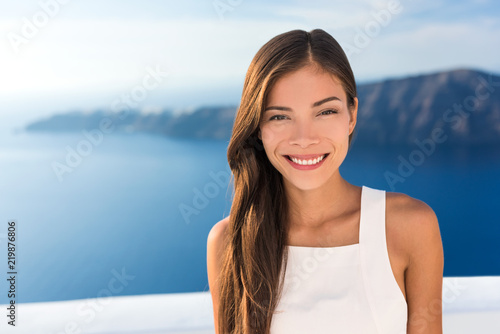 Beautiful Asian young woman smiling portrait in sunshine. Gorgeous Chinese Caucasian model in summer outdoors, Europe travel destination, luxury Santorini Greece getaway.