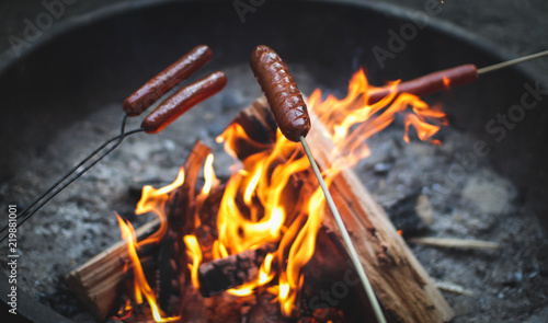 hotdogs roasting on sticks over flames in a campfire