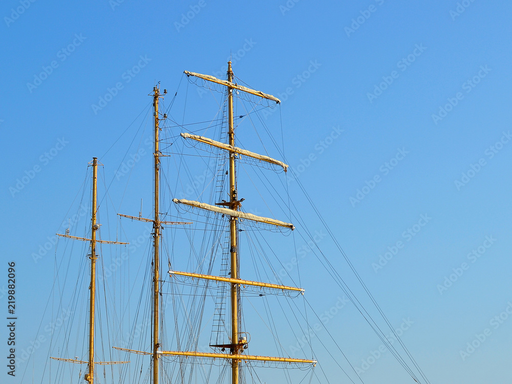 Three masts of a sailing ship with folded up sails and shrouds against a blue summer sky, copy space Three masts of a sailing ship with folded up sails and shrouds against a blue summer sky, copy space