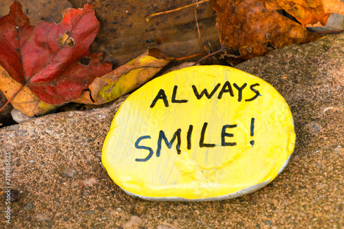 A yellow hand painted flat stone with words 'always smile!' photo