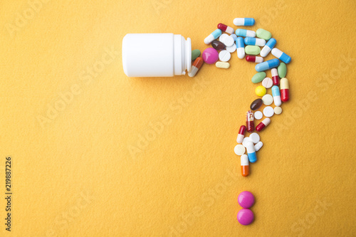 Pills or capsules as a question mark and white plastic bottle. photo