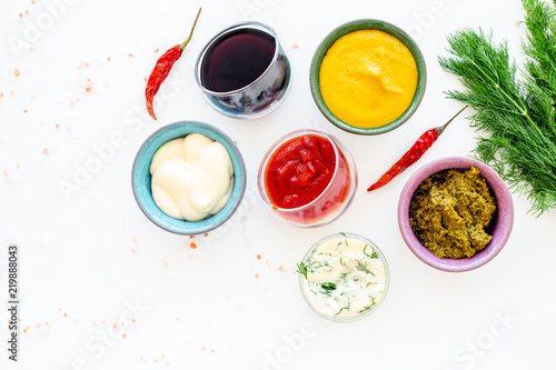 Different dip sauce in bowls near chili pepper and greenery. Ketchup, mayonnaise, mustard, soy sauce, barbecue sauce, pesto, mustard, sour on white background top view copy space