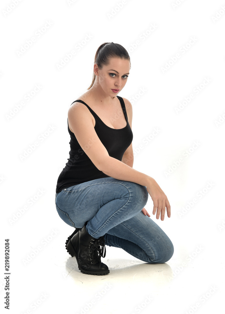 full length portrait of brunette girl wearing black single and jeans. seated pose. isolated on white studio background. full length portrait of brunette girl wearing black single and jeans. seated pose. isolated on white studio background.