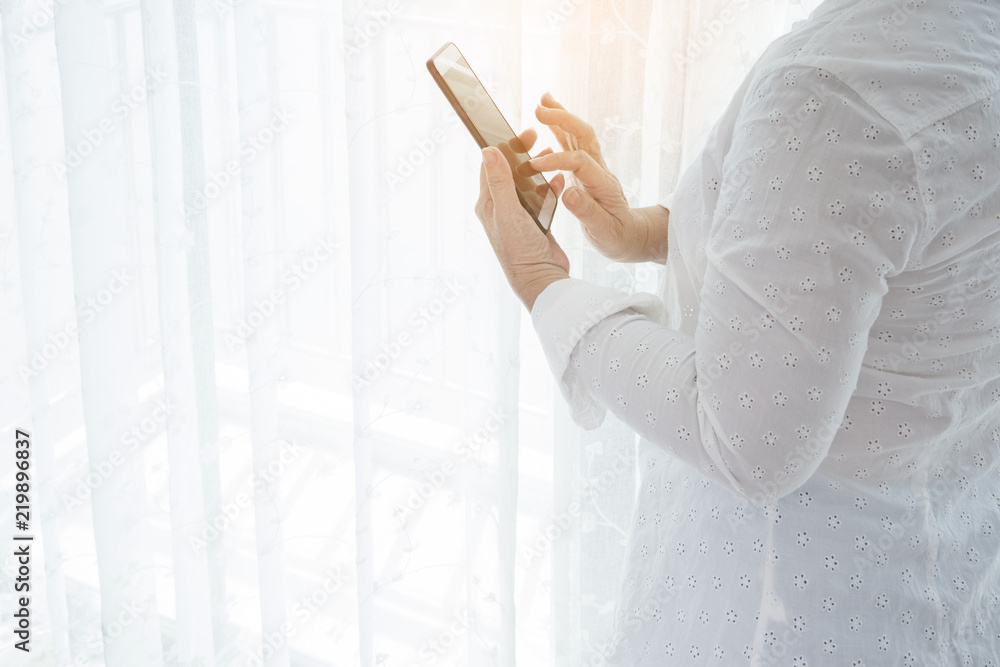 Woman standing and using modern smartphone near window