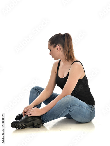 full length portrait of brunette girl wearing black single and jeans. seated pose. isolated on white studio background. photo