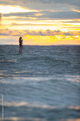 Beautiful woman stand up paddle boarding at sunrise or sunset