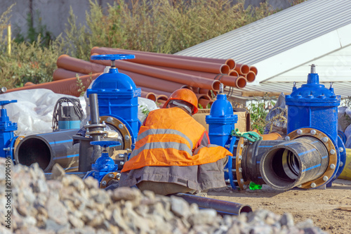 Worker at the construction site assembly elements of the pipeline, plastic pipes, cast iron valve.