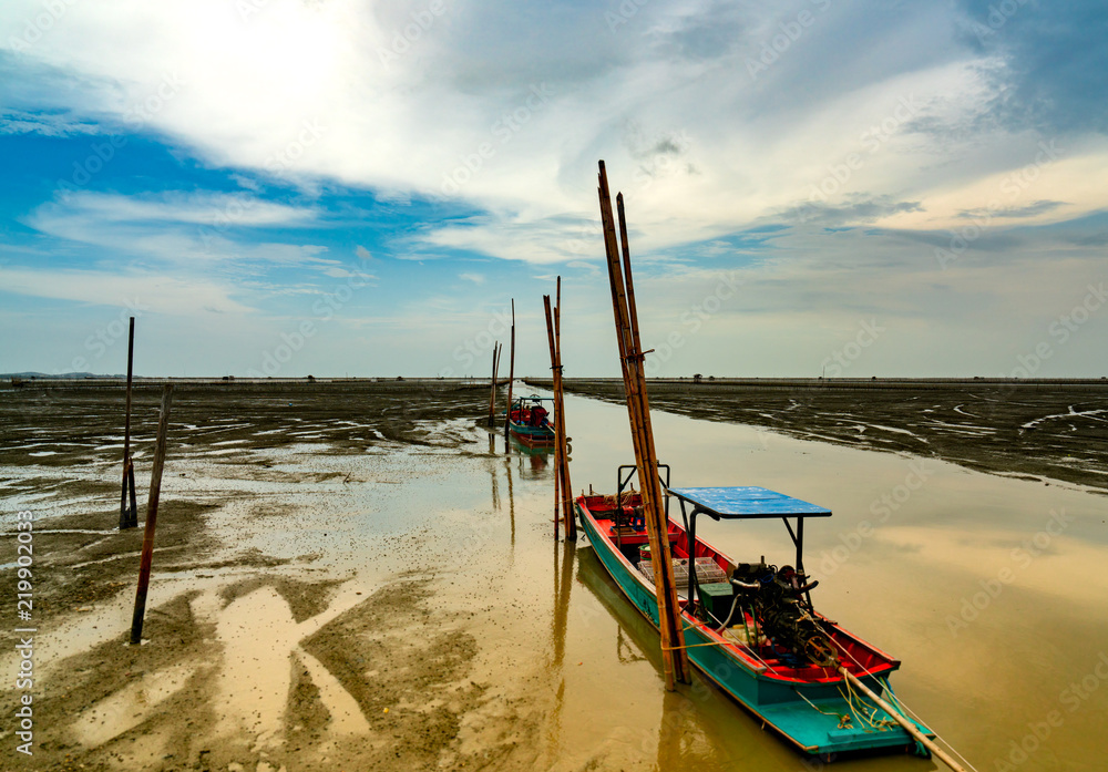 Fisherman's boat parked at coastal mud flat at tide. Landscape of sea and beautiful blue sky and white clouds at sunset. Mud beach.