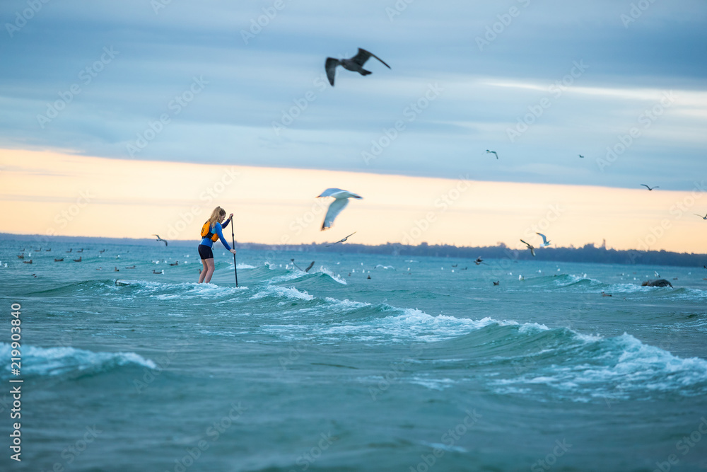 Beautiful woman stand up paddle boarding at sunrise or sunset