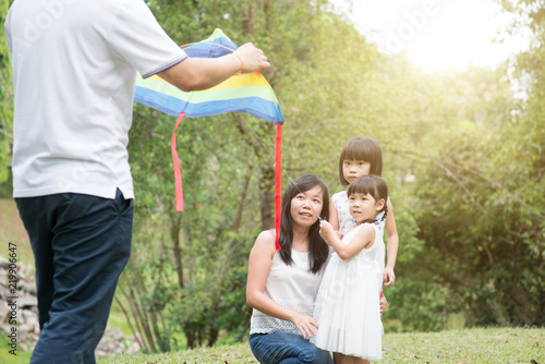 Asian family flying kite outdoors.