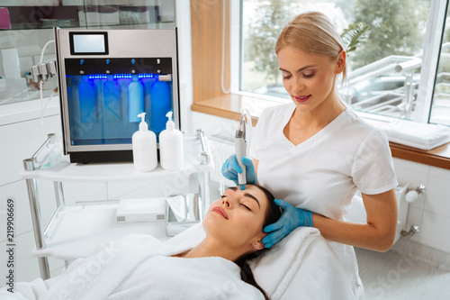 Professional skills. Professional skilled cosmetologist standing near the client while doing hydrafacial procedure