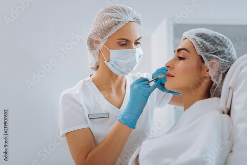 Skin renewal. Professional female cosmetologist standing near her client while doing a beauty injection for her