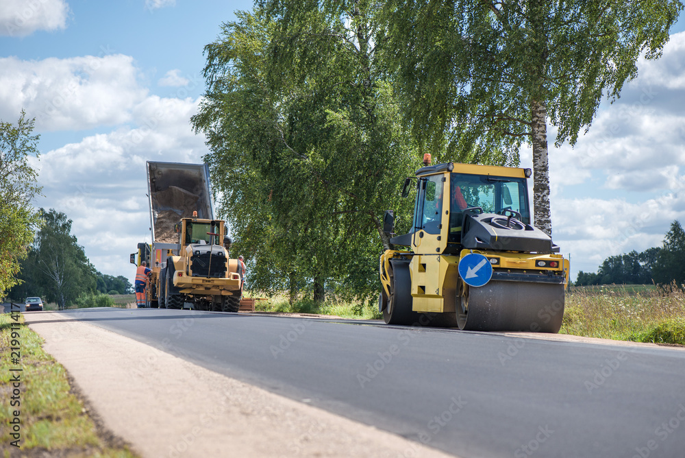 Road construction workers repairing highway road on sunny summer day. Loaders and trucks, heavy vibration roller compactor with arrow road sign on newly made asphalt. Work inspection with drone