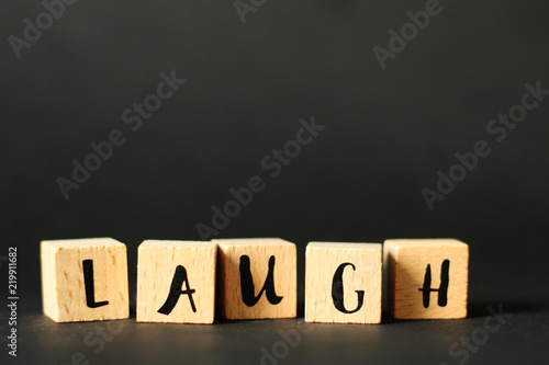 LAUGH - word created from wooden cubes with letters, selective focus, black background, free copy space