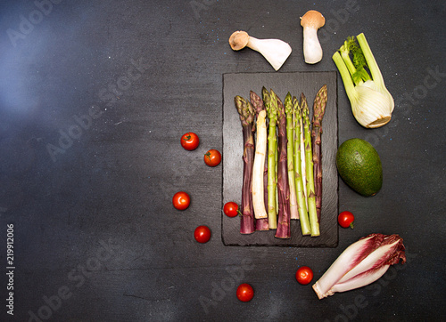 Ingredients for preparing healthy meal. Cherry tomato, asparagus, cherry tomatoes, chicory, fennel, avocado, oyster mushrooms over on black background. Flat lay. Overhead. Copy space.