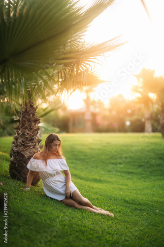 Beautiful brunette sitting on grass near the palm