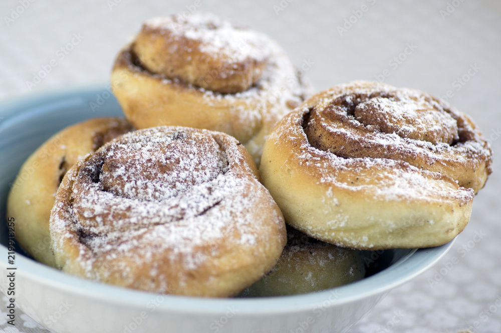 Cinnamon snails called kanelbullar, very tasty sweet rolls in blue bowl on floral pattern tablecloth