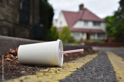 Discarded drinks container lying at the edge of an urban street with car in the distance
