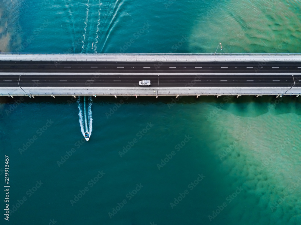 Car crosses bridge as speed boat travels under it.  Scenic aerial view with copy space