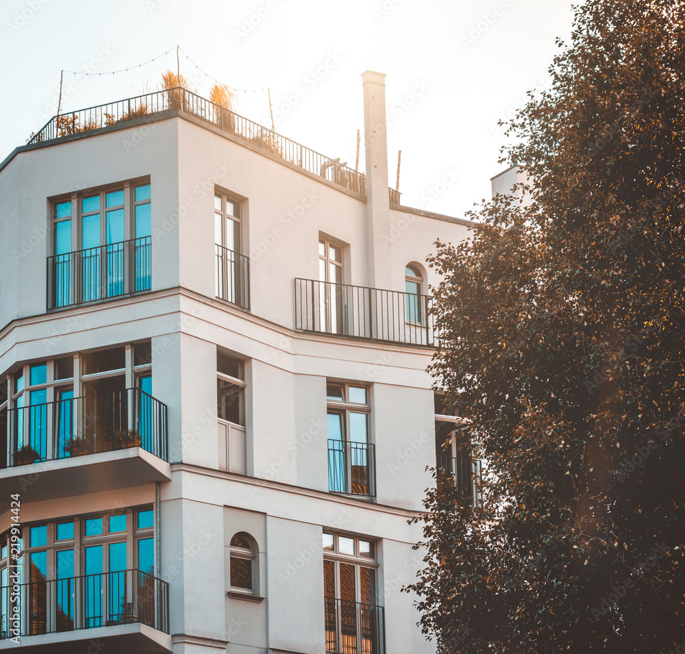 Obraz premium square picture of modern apartment building with white facade and green tree on the side