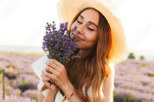 Cheerful young girl in straw hat smeling lavender bouquet photo