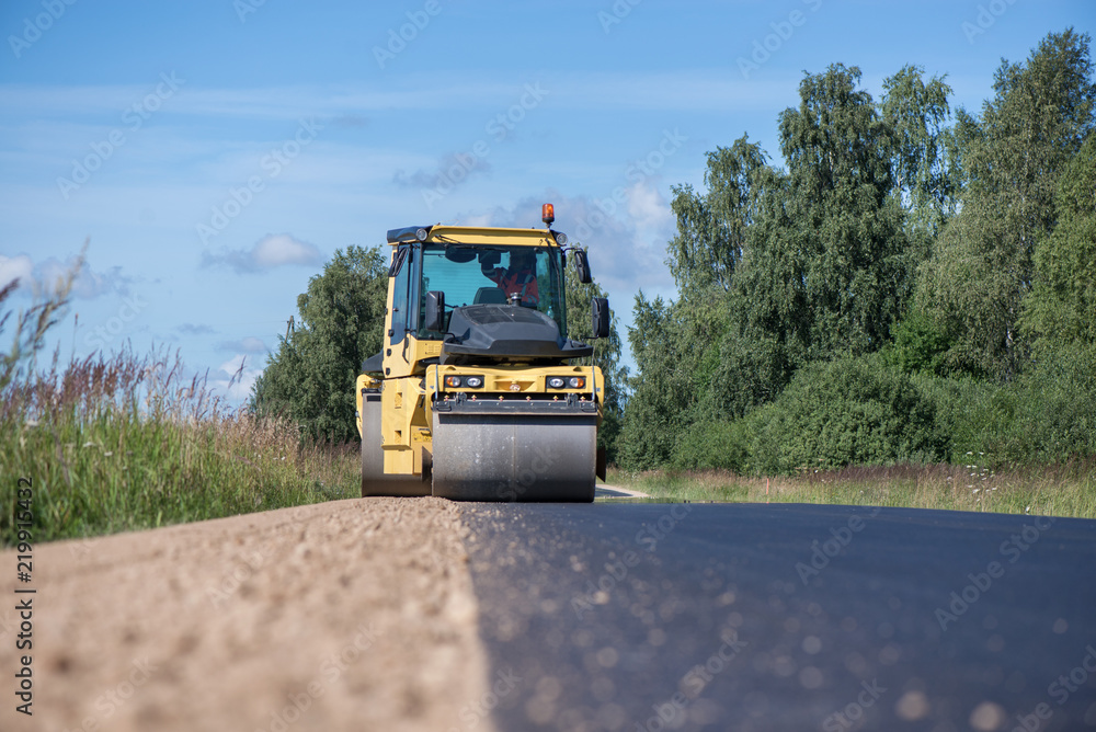Yellow heavy vibration roller at asphalt pavement works. Road repairing in city. Road construction workers repairing highway road on sunny summer day. Heavy machinery, loaders and trucks Yellow heavy vibration roller at asphalt pavement works. Road repairing in city. Road construction workers repairing highway road on sunny summer day. Heavy machinery, loaders and trucks