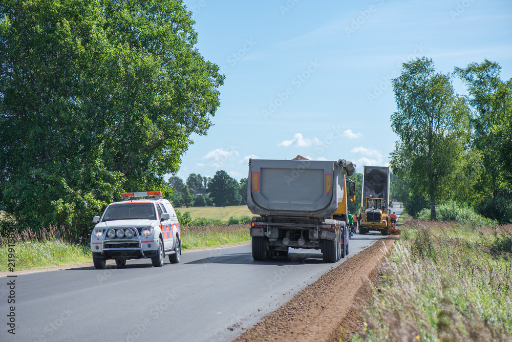 Road construction workers repairing highway road on sunny summer day. Loaders and trucks on newly made asphalt. Heavy machinery working on street. Road curbs being constructed with gravel